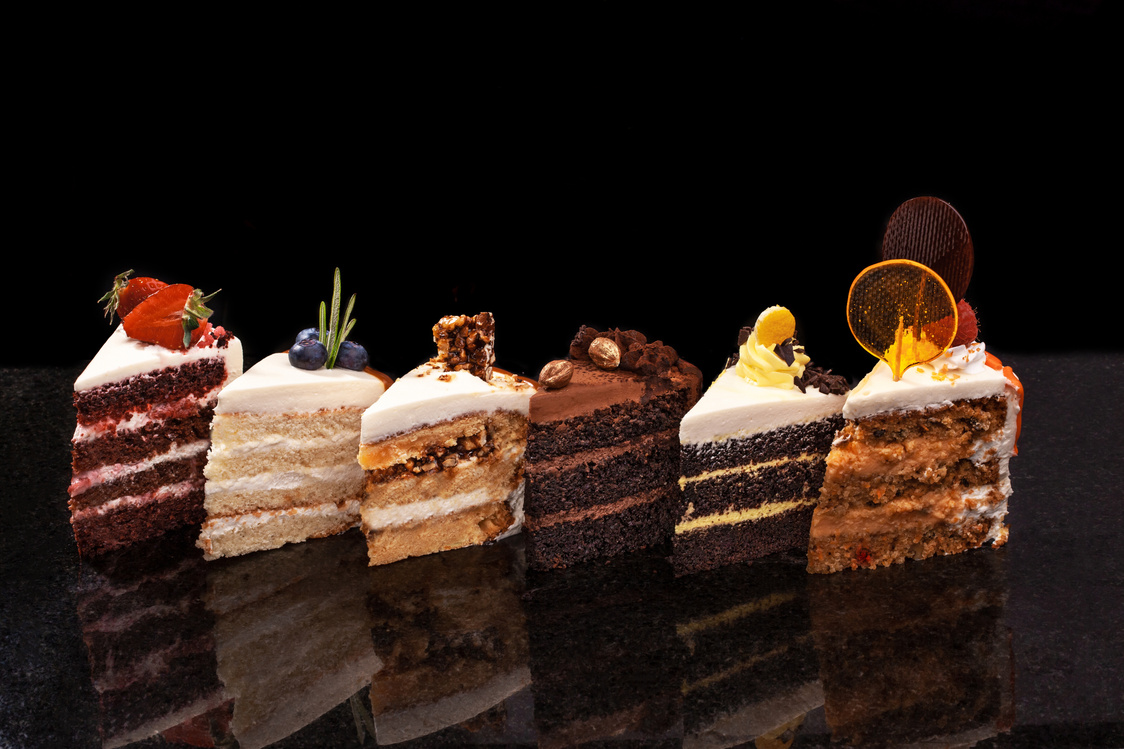 Assorted large pieces of different cakes: chocolate, raspberries, strawberries, nuts, blueberries. Pieces of cakes on a black table